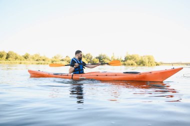 Sakin bir gölde kanoyla kürek çeken bir adam, su sporları ve açık hava eğlenceleriyle uğraşırken doğanın huzurunun tadını çıkarıyor.