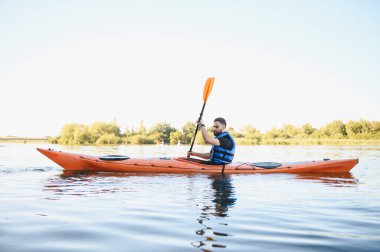 Huzurlu bir nehirde kanoyla kürek çeken bir adam, doğanın güzelliğinin ortasında aktif bir eğlence ve yaz güneşini kucaklıyor.