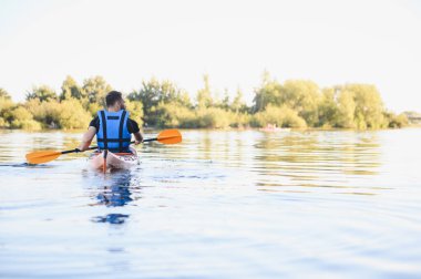 Sakin bir gölde kano süren bir adam, doğanın huzurunun tadını çıkarıyor ve aktif olarak dinleniyor.