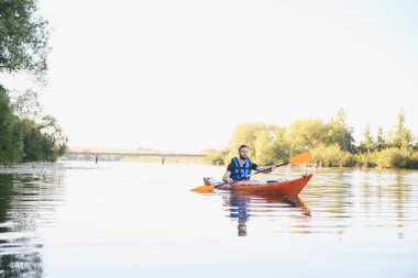 Sakin bir nehirde kano süren bir adam, doğanın huzurunun tadını çıkarıyor ve aktif olarak dinleniyor.