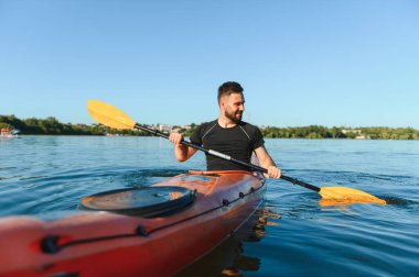 Genç bir adam güneşli bir gölde kayak yapıyor, su sporlarının heyecanını kucaklıyor ve açık havada hareketli bir günün tadını çıkarıyor.