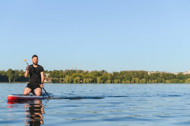Genç sporcu, güneşli bir yaz gününde sakin bir gölde, yemek masasında kürek çekerek doğanın huzurunun tadını çıkarıyor.