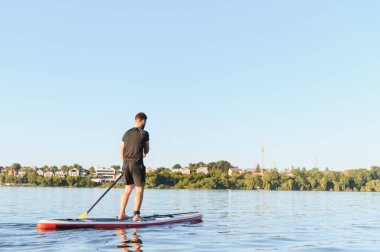 Şehir manzarasında sakin bir gölde, yemek masasında kürek çeken sporcunun arka görüntüsü, su sporu ve aktif eğlence.
