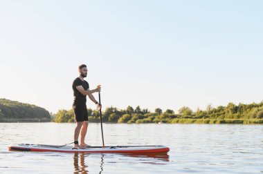 Yemek masasında dengede duran genç sporcu, gün batımında çevresi doğa ile çevrili sakin bir gölde kürek çekiyor, rahatlatıcı bir su sporu aktivitesinin keyfini çıkarıyor.