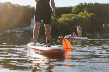 Adam yemek masasında kürek çekiyor, gün batımında gölde aktif bir dinlenme anının tadını çıkarıyor.
