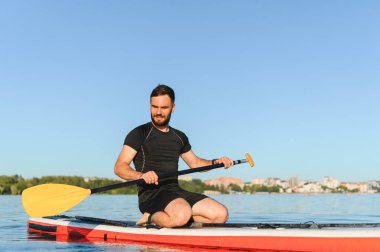 Genç sporcu yemek masasında diz çöküp yazın bir gölde yüzüyor ve son moda bir su sporu yapıyor.