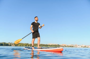 Genç sporcu yemek masasında kürek çekiyor, gölde güneşli bir günün tadını çıkarıyor, su sporu yapıyor ve aktif olarak dinleniyor.
