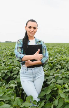 Kendine güveni tam bir kadın tarım uzmanının elinde bir pano ve tohum ekilmiş soya tarlasında dikilirken başparmak hareketi.