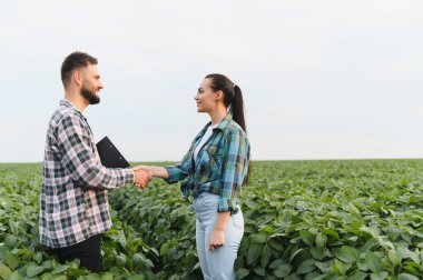 Soya tarlasında tokalaşan iki çiftçi, tarım sektöründe başarılı bir iş anlaşmasını kutluyor.