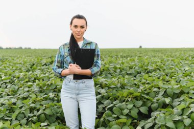 Genç tarımcı elinde bir pano, ekilmiş tarlalarda soya bitkilerinin büyümesini denetliyor, sağlıklı hasat sağlıyor.
