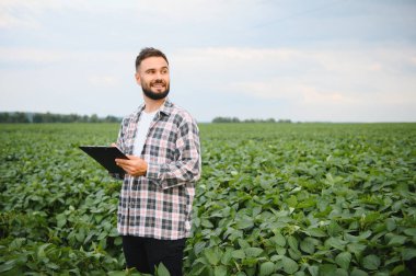 Ekinleri inceleyen ve soya fasulyesi tarlasında notlar alan tarımcı sağlıklı büyümeyi ve verimi en üst düzeye çıkarmayı garanti ediyor.