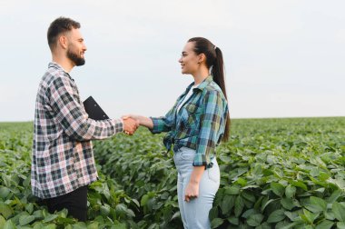 Canlı bir soya tarlasında tokalaşan çiftçiler başarılı bir iş anlaşmasını kutluyor ve güçlü bir ortaklığı teşvik ediyor.