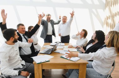 Hevesli iş ekibi olumlu sonuçları kutluyor, ofis toplantısı sırasında heyecanla el kaldırıyor.