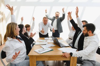 Hevesli iş ekibi olumlu sonuçları kutluyor, kollarını kaldırıyor ve verimli bir ofis toplantısında başparmak kaldırıyor.