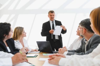 Deneyimli bir işadamı modern bir ofiste bir şirket toplantısında ekibini başarıya götüren bir belge sunuyor.