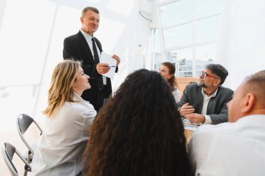 Kıdemli müdür, parlak ve modern bir ofiste verimli bir toplantı sırasında ekibine yeni iş stratejisini sunuyor.