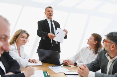 İş adamları, modern bir ofiste yaptıkları toplantıda liderlerini yeni bir projeyi anlatırken dinliyor.