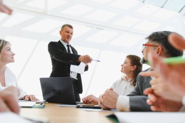 İşletme ekibi liderleriyle bir tartışmaya giriyor, ofiste dinamik bir şirket toplantısı sırasında iş stratejilerini detaylandırıyor.