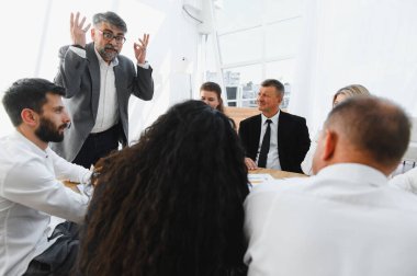 Üst düzey yönetici, modern ofis ortamındaki bir toplantıda iş stratejisini açıklarken takım üyeleriyle takılıyor.