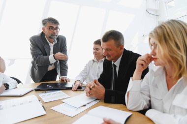 Kıdemli işletme müdürü ekibiyle verimli bir tartışma yürütüyor, raporları analiz ediyor ve modern bir ofiste başarı stratejisi geliştiriyor.