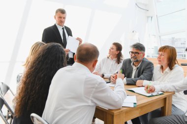 İş adamları, modern bir ofiste yapılan verimli bir toplantıda liderlerinin yeni bir stratejiyi açıklamasını dinliyor.