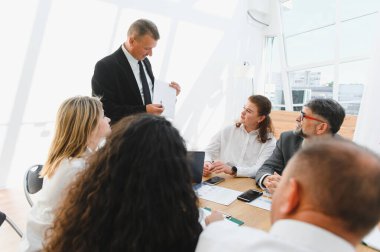 İş dünyası lideri, modern bir ofiste verimli bir toplantı sırasında meslektaşlarına iş stratejisini anlatıyor, işbirliği ve başarıyı teşvik ediyor.