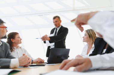 Üst düzey yönetici şirket toplantısında iş stratejisini açıklarken bir çizelge ve kalem kullanıyor.