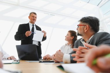 İş adamları, modern bir ofiste yapılan verimli bir toplantıda liderlerini bir projeyi anlatırken dinliyor.