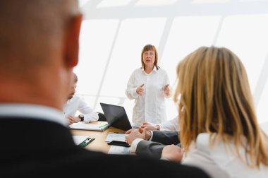 Dinamik bir iş toplantısına liderlik eden kadın yönetici, ekibiyle parlak, modern bir ofis ortamında temas kuruyor, işbirliği ve yeniliği teşvik ediyor.