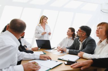 Kadın yönetici, parlak ve modern ofis ortamındaki vizyon ve uzmanlığıyla meslektaşlarına ilham veren bir takım toplantısına liderlik ediyor.