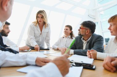 Modern ofis ortamında bir şirket toplantısı sırasında stratejik tartışmalara giren iş ekibi, işbirliğini ve planlamayı teşvik ediyor.