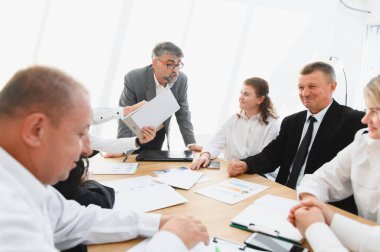 İşletme ekibi şirket toplantısı sırasında belgeleri analiz ederken, lider bir projeyi açıkladı.