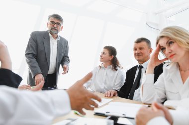 Modern bir ofiste şirket toplantısına katılan iş adamları, yeni bir stratejiyi açıklayan üst düzey yöneticilerini dinliyorlar.