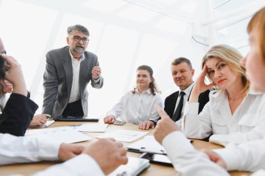 İş adamları, modern bir ofiste, parlak doğal ışıkla dolu gergin bir toplantıda üst düzey yöneticilerini dikkatle dinliyorlar.