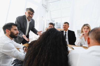 Tecrübeli yönetici bir ofis toplantısında iş stratejisini ekibe açıklıyor, işbirliğini teşvik ediyor ve başarılı oluyor.