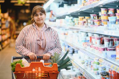 Genç Hintli bir kadın markette alışveriş arabasını itiyor, süt ürünlerini seçiyor.