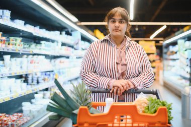 Genç Hintli bir kadın marketin koridorlarında gezinirken içi taze yiyecek dolu bir alışveriş arabasını itiyor.
