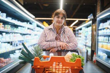 Genç Hintli bir kadın marketin koridorlarında dolaşırken içi taze yiyeceklerle dolu bir alışveriş arabasını itiyor.