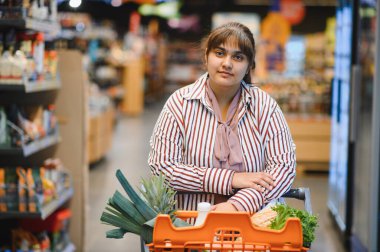 Genç Hintli bir kadın süpermarkette alışveriş yaparken içi taze meyve ve sebze dolu bir alışveriş arabasını itiyor.