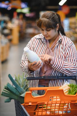 Genç Hintli kadın marketten alışveriş yaparken süt şişesindeki malzemeleri kontrol ediyor.