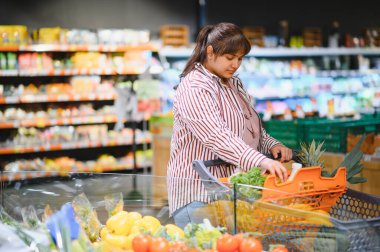 Genç Hintli bir kadın alışveriş arabasını iterken canlı bir süpermarket koridorunda rengarenk ürünler seçiyor.