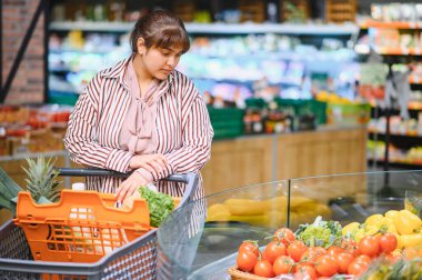 Genç Hintli bir kadın canlı bir süpermarkette canlı sebze seçerken renkli bir ürün dizisiyle çevrili olarak taze sebze seçiyor.