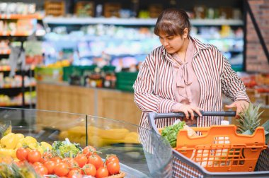 Genç Hintli kadın alışveriş arabasını iterken markette taze sebze seçiyor, sağlıklı bir yaşam tarzının tadını çıkarıyor.