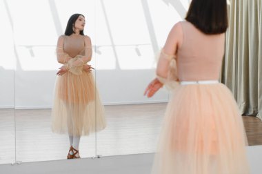 Şeftali tütütüyle dans stüdyosundaki aynanın önünde bale çalışması yapan genç bir kadın koreografisini prova ediyor.