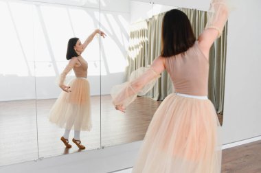 Genç balerin dans stüdyosunda bale çalışıyor. Tekniğini geliştirmek için ayna kullanıyor.