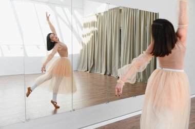 Genç balerin dans stüdyosunda bale çalışıyor. Tekniğini geliştirmek için ayna kullanıyor.