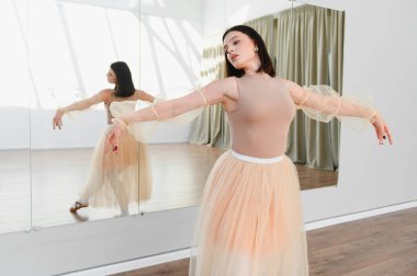 Genç balerin dans stüdyosunda bale çalışıyor, etek giyiyor ve yansımasına odaklanıyor.