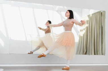 Dans stüdyosunda bale eğitimi alan genç bir kadın aynanın önünde prova yapıyor.