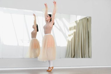 Genç balerin dans stüdyosunda büyük bir ayna ve perdelerle dans ediyor. Zarafet ve adanmışlık sergiliyor.