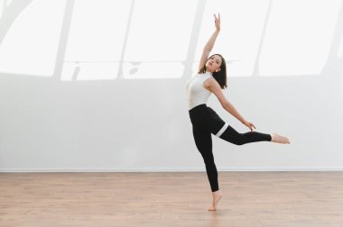 Parlak bir stüdyoda modern bir dans gösterisi sergileyen zarif dansçı, esneklik ve sanatsal ifade sergiliyor.